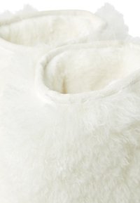 Biały, miękki kapcie z wełny o zaokrąglonym kształcie. Charakteryzuje się zakrzywionymi krawędziami i pluszową, futerkową powierzchnią dla komfortu.