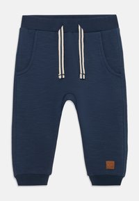 Mørkeblå joggebukser laget av teksturert stoff. Har to lommer, elastisk midje med snor og ribbestrikkede mansjetter. Lærlogo-patch.