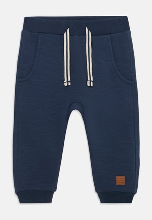 Mørkeblå joggebukser laget av teksturert stoff. Har to lommer, elastisk midje med snor og ribbestrikkede mansjetter. Lærlogo-patch.