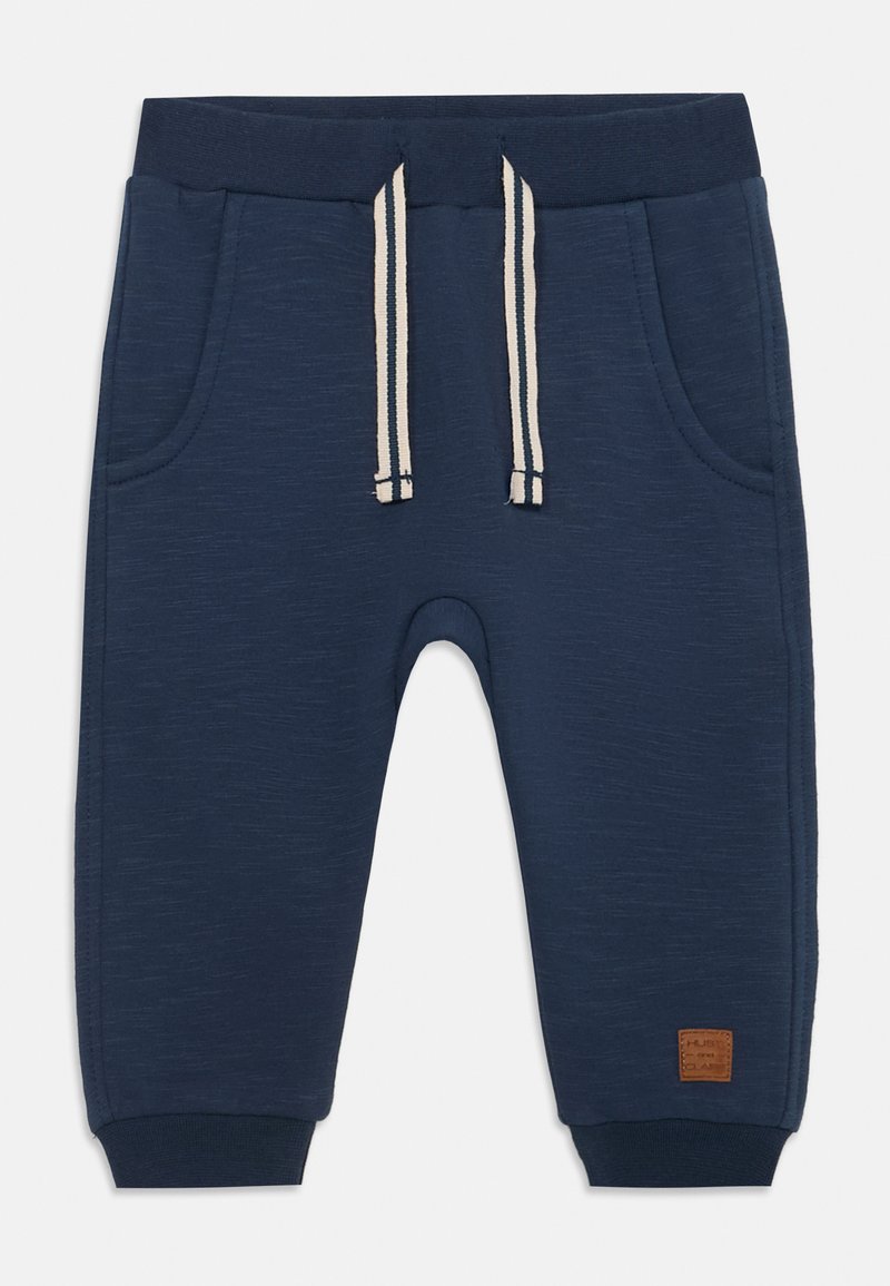 Mørkeblå joggebukser laget av teksturert stoff. Har to lommer, elastisk midje med snor og ribbestrikkede mansjetter. Lærlogo-patch.