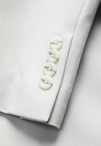 Helehall kangasvarrukas, sileda tekstuuriga, millel on neli valget nuppu peene marmoreeritud mustriga. Nähtavad korrektsed õmblusdetailid.