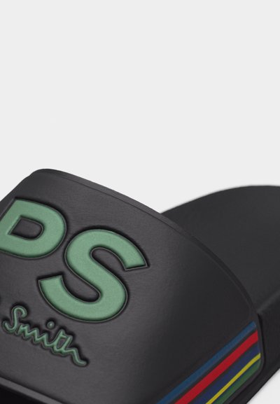 Μαύρο σανδάλι με φάσα, με ανάγλυφα πράσινα γράμματα "PS" και υπογραφή, που διαθέτει κόκκινες, μπλε, κίτρινες και πράσινες ρίγες στο πλάι της φάσας.