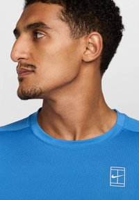 Maglietta sportiva blu in tessuto traspirante con scollatura rotonda. Presenta un piccolo logo bianco di Nike sul lato sinistro del petto.