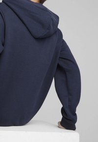 Felpa con cappuccio blu navy, maniche lunghe, polsini a coste e vestibilità comoda; tessuto liscio senza motivi o loghi visibili.