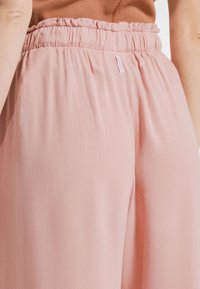 Ljusrosa byxor med ett texturerat tyg. Har en rynkad midjeresår och en liten varumärkesetikett fäst framtill.