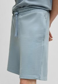 Shorts bleu clair en tissu doux. Présentent une taille élastique avec cordon de serrage et des poches latérales. Logo "HUGO" brodé sur la jambe.