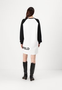 Vestuário de moletão oversized em preto e branco com mangas raglan e impressão "GARFIELD" na bainha. Modelo usa botas pretas até ao joelho.