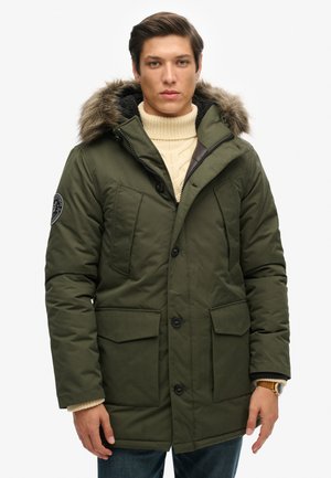 Parka verde con capucha forrada de pelo, cierre delantero de botones, dos grandes bolsillos frontales y un forro interior texturizado.
