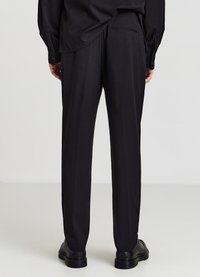 Schwarze maßgeschneiderte Hose mit gerader Beinform, glatter Textur, ausgestattet mit seitlichen Taschen und einer dezenten Gesäßtasche, kombiniert mit schwarzen Schuhen.