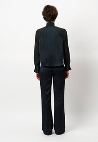 Zwarte zijden blouse met een hoge kraag en lange mouwen, gecombineerd met bijpassende hoge taille, wijde broek. Soepele textuur, minimalistisch ontwerp.
