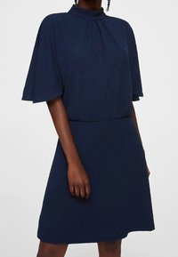 Robe bleu marine avec manches courtes volantées, col montant et détail froncé. Confectionnée dans un tissu doux avec une silhouette simple et fluide.