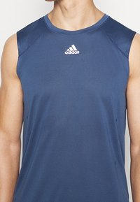 Námořnicky modré sportovní tílko, lehká látka, bez rukávů, kulatý výstřih, na hrudi bílý logo Adidas, strukturovaný materiál.