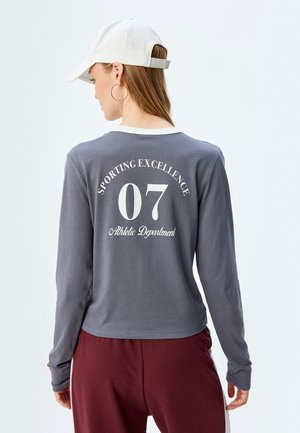Long-sleeve, gray athletic shirt with white lettering "SPORTING EXCELLENCE 07 Athletic Department." Features a rounded hem and crew neck.