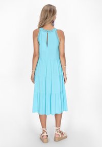 O rochie fără mâneci, de culoare albastră deschisă, cu o fustă în straturi, detalii elegante la spate și o deschidere în formă de cheie la spate.