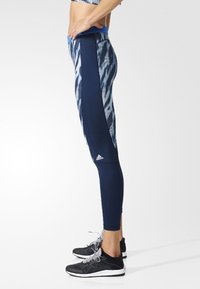 Marineblaue Leggings mit strukturiertem Muster und schwarzen Seiteneinsätzen, ausgestattet mit einem elastischen Bund und einem Logo-Detail in der Nähe des Knöchels.