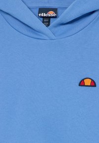 Ljusblå huvtröja i mjukt tyg med en broderad logotyp i rött, gult och svart. Designen inkluderar en huva och ribbad krage.