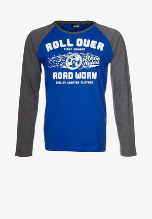 Chemise bleue à manches longues avec des manches gris foncé, avec un texte blanc : « Roll Over », « Storm Riders », « Road Worn » et un graphique d'une roue tournante.