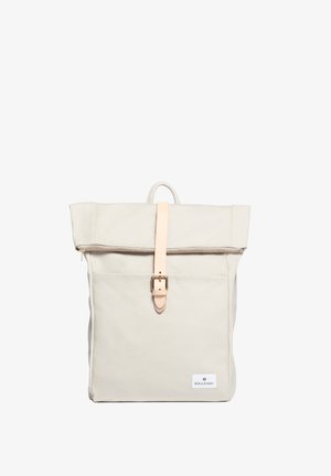 Sac à dos en toile beige clair avec un design à rabat, maintenu par une sangle en cuir rose et une boucle en métal. Comprend une poche avant et une étiquette de logo.