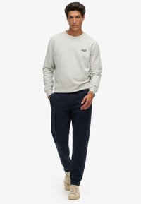 Grijze sweatshirt met een ronde hals, voorzien van een klein logo. Gecombineerd met marineblauwe joggers en beige sneakers. Eenvoudig en casual ontwerp.