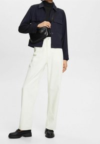 Mörkblå jacka med två framfickor, vita högmidjade byxor och svarta skor. Outfiten har en svart tvärmonterad väska.