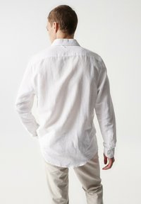 Camisa blanca de manga larga hecha de lino, con cuello abotonado y un corte relajado, con dobladillo curvado y tejido texturizado.