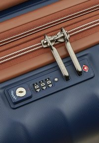 Maleta de color azul oscuro con una superficie texturizada, cremalleras de bronce, cerradura de combinación y una cerradura de llave plateada. Marca Delsey en la cremallera.