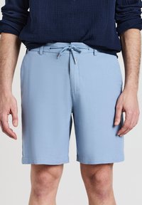 Helle blaue Shorts aus strukturiertem Material mit einem Kordelzugbund und Fronttaschen, die einen sauberen Schnitt und eine Länge bis zur Mitte des Oberschenkels aufweisen.