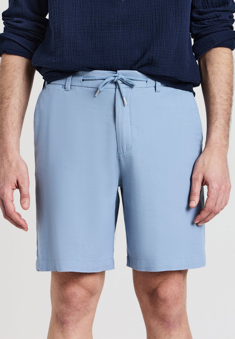 Helle blaue Shorts aus strukturiertem Material mit einem Kordelzugbund und Fronttaschen, die einen sauberen Schnitt und eine Länge bis zur Mitte des Oberschenkels aufweisen.