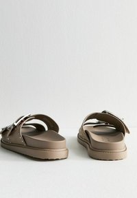 Sandales en caoutchouc marron avec deux larges sangles, ferrures en argent et semelles texturées. Semelle intérieure légèrement rembourrée avec de petits trous d'accent.