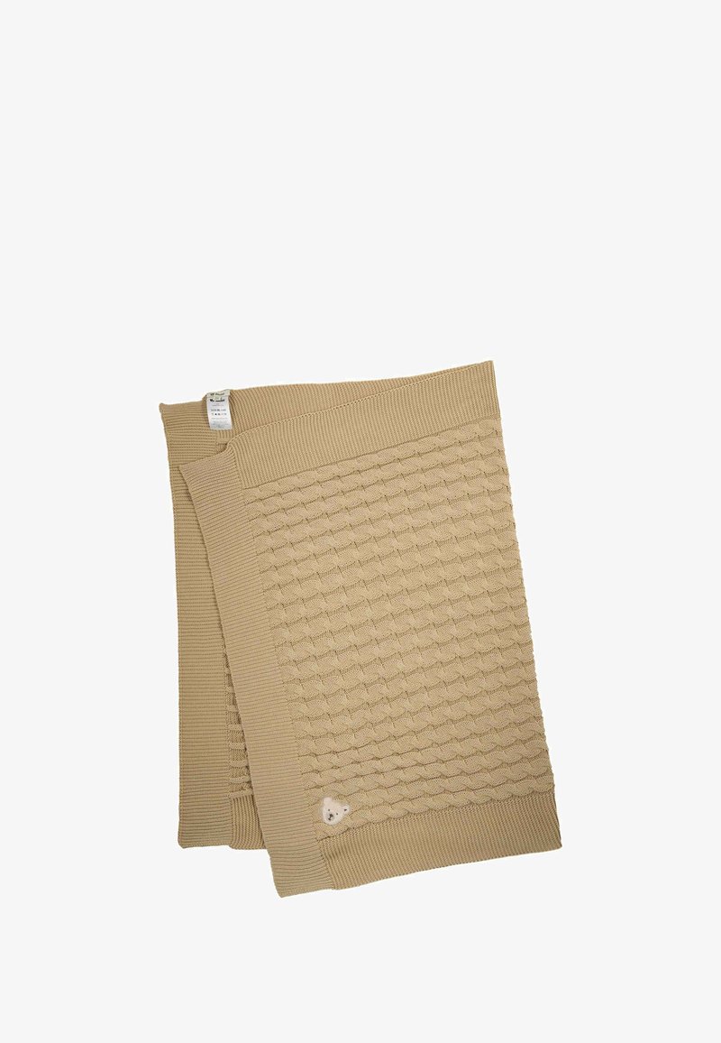 Béžová pletená deka s texturovaným vzorem a hladkým okrajem, s malou teddy medvědí dekorací v jednom rohu.