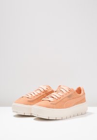 Růžové semišové tenisky s texturovaným bočním panelem, silnou bílou podrážkou a plochými tkaničkami. Na boční straně mají stříbrné logo.