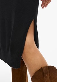 Svart stickad klänning med sidosprund, ribbad textur vid fållen och matchande bruna mockastövlar som går över knäna.