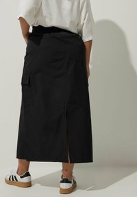 Svart midi kjol med en sidoklyfta och cargo fickor, tillverkad av lättviktigt tyg. Bärs med vita sneakers med svarta ränder.