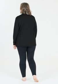 Sort langærmet top med en afslappet pasform, parret med ribbede sorte leggings, begge med glat tekstur og ensfarvet design.