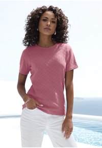 Kurze Ärmel, korallenrotes T-Shirt mit einem strukturierten geometrischen Muster, Rundhalsausschnitt und lockerer Passform, kombiniert mit weißen Hosen.