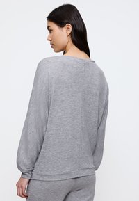 Felpa grigia a maniche lunghe con vestibilità rilassata, polsini a coste e una texture liscia, caratterizzata da un ampio scollo e senza motivi visibili.