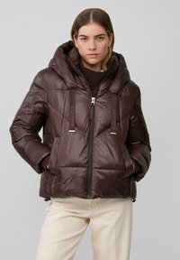 Braune Steppjacke mit hohem Kragen und verstellbarer Kapuze. Mit Reißverschluss, zwei Vordertaschen und glänzendem Finish.