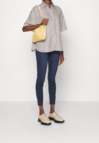 Randig kortärmad skjorta, blå skinny jeans, krämfärgade oxfordsko och en gul axelväska. Enkel design med kontrasterande färger och texturer.