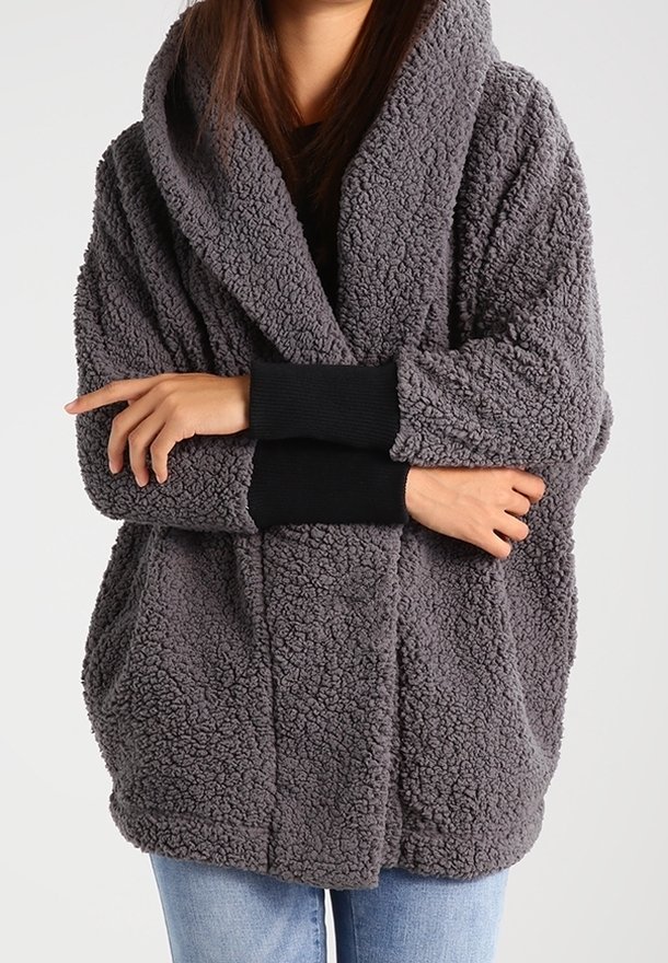 Giacca con cappuccio in pile grigia, dalla superficie morbida e testurizzata, vestibilità oversize, tasche frontali e polsini a coste neri.