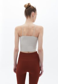 Světle šedý upnutý crop top s tenkými ramínky, doplněný vysokými legínami v měděné barvě s texturovaným vzorem po celé ploše.