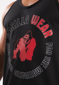 Zwarte mouwloze tanktop met een rood gorilla-graphic en witte tekst die "GORILLA WEAR FOR THE MOTIVATED" leest, met bijpassende details.