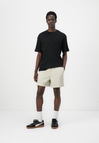 T-shirt noir à manches courtes côtelé, shorts beiges, baskets noires avec accents gris, associées à des chaussettes blanches à la cheville. Design simple et moderne.