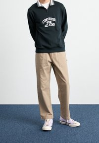 Donkergroen sweatshirt met witte print "Converse All Star", gestreepte kraag, gecombineerd met beige broek en lila sneakers. Rechte pasvorm.