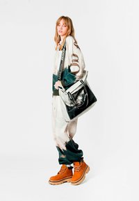 Sudadera extragrande multicolor con diseño de bosque, pantalones deportivos a juego y botas naranjas. Bolsa negra con detalles estampados.