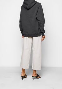 Felpa grigia con cappuccio e vestibilità rilassata, abbinata a pantaloni larghi color crema e sandali neri con dettagli a fiocco.