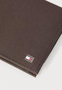 Portefeuille marron texturé avec une finition lisse. Présente un petit accent de logo en rouge, blanc et bleu dans le coin.
