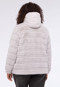 Jasnoszara kurtka z sztucznego futra z poziomą teksturą w paski, z ocieplaną kapturem i luźnym fasonem, posiadająca długie rękawy i boczne kieszenie.