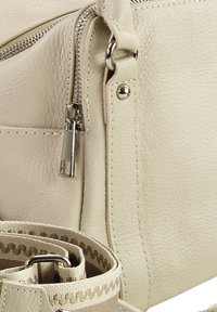 Beige leren tas met een textuur, voorzien van een zilverkleurige rits, een afneembare riem met een patroonaccent en opvallende stiknaden.