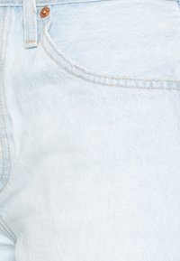 Lichtblauwe spijkerbroek van denim met een gladde textuur, voorzien van oranje stiknaden en koperen klinknagelaccenten op de tailleband en zak.