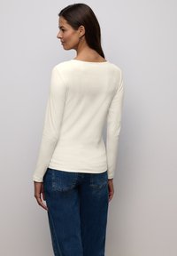 Kremowy top z długim rękawem i prążkowanym materiałem, zestawiony z niebieskimi jeansami. Top ma zaokrąglony dekolt i dopasowany krój.